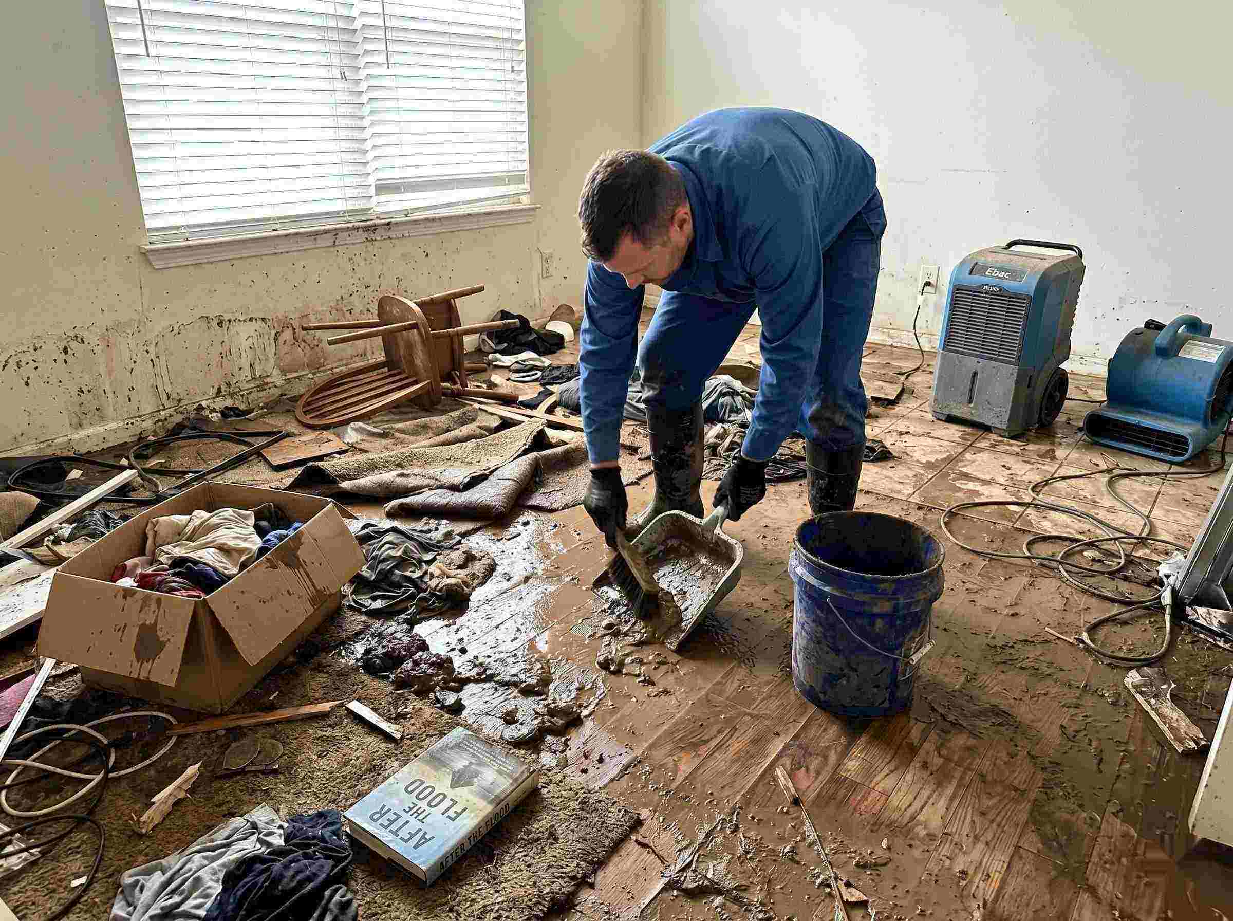 Realistic photo of a technician performing mud and debris removal after a home flood in Chesapeake, showing soaked furniture, wet flooring, and scattered debris during post-flood cleanup.